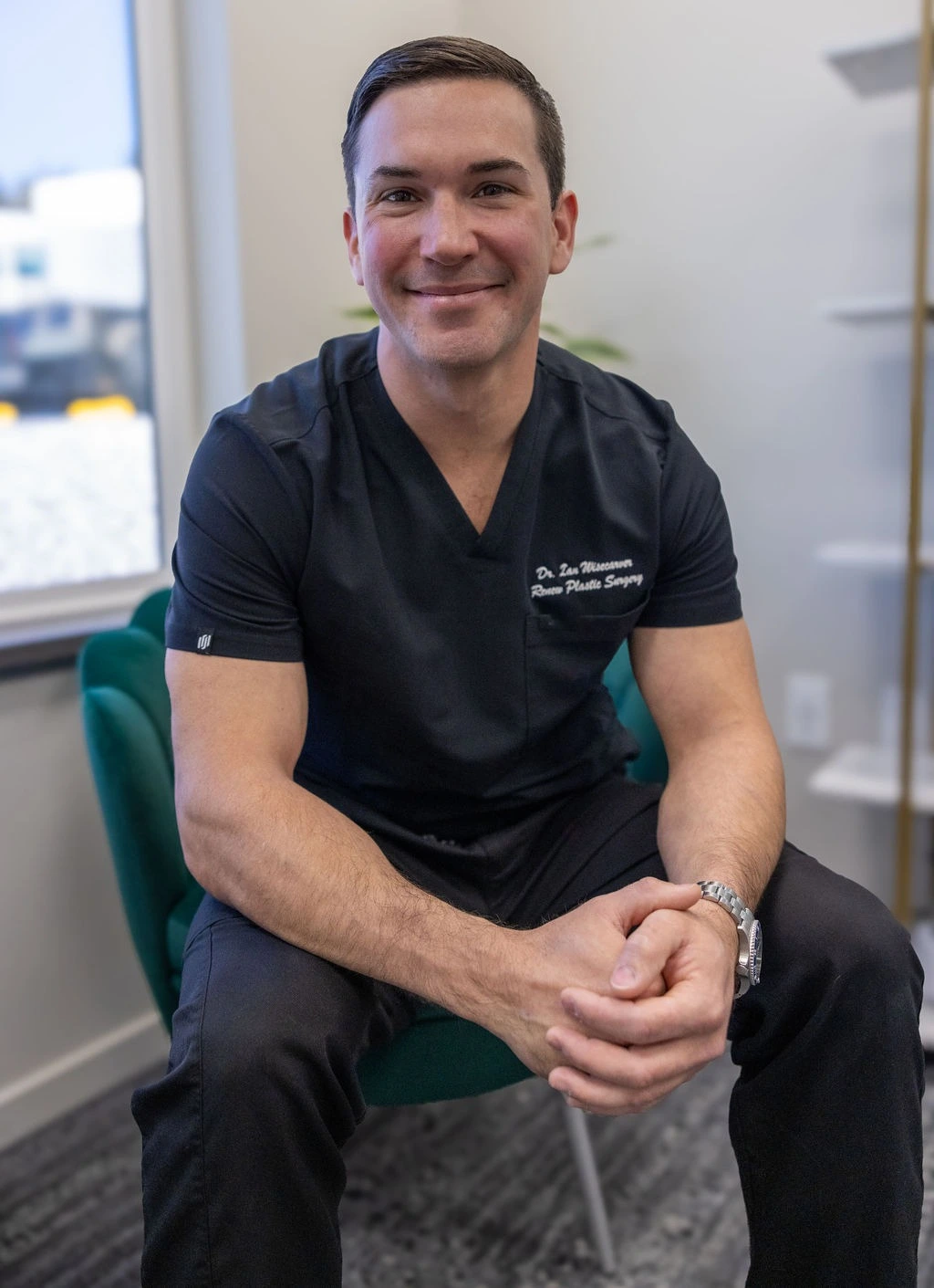 Smiling male doctor with short brown hair and brown eyes, wearing a black scrub top.